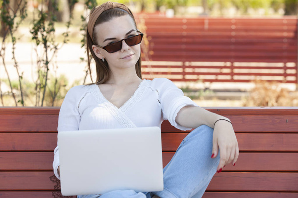 Young girl on a bench with a laptop. - Фото, изображение