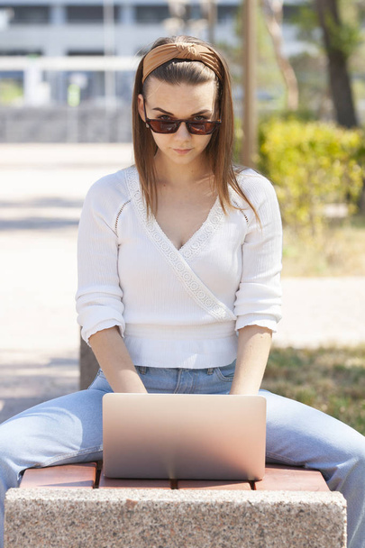 Beautiful woman sitting on a park bench using a laptop. - Photo, image