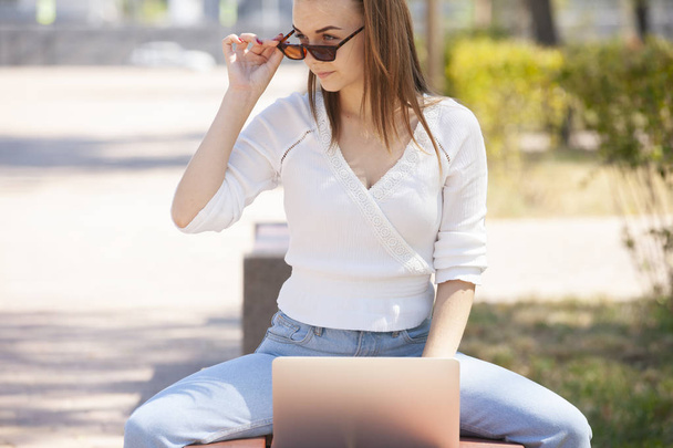 Beautiful woman sitting on a park bench using a laptop. - Zdjęcie, obraz