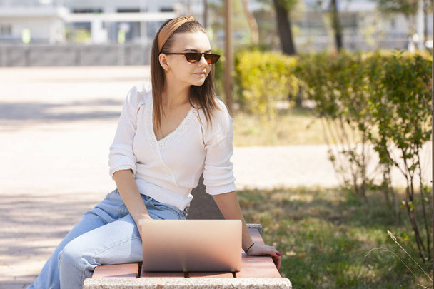 Beautiful woman sitting on a park bench using a laptop. - Fotoğraf, Görsel