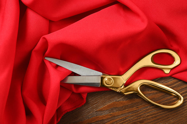 Red fabric and sharp scissors on wooden table, flat lay - Foto, imagen
