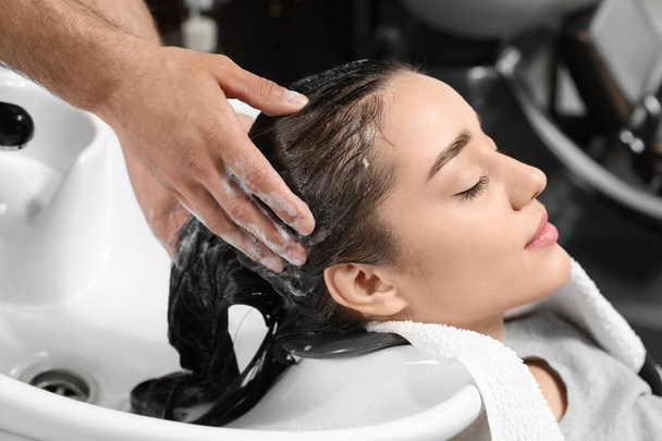 Stylist washing client's hair at sink in beauty salon - Photo, image
