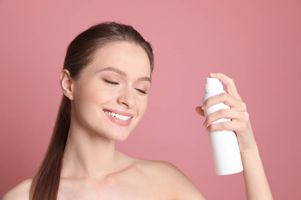 Young woman with bottle of thermal water on color background. Cosmetic product - Foto, Imagem