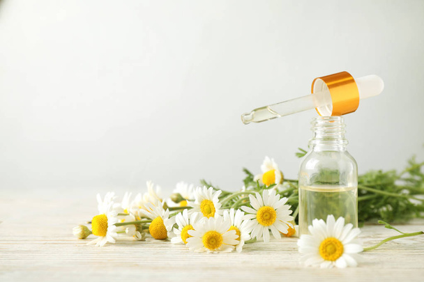 Bottle of chamomile essential oil and flowers on white table, space for text - Photo, image