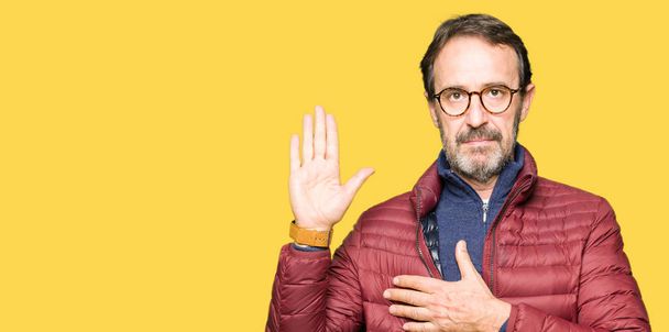 Middle age handsome man wearing glasses and winter coat Swearing with hand on chest and open palm, making a loyalty promise oath - Photo, Image