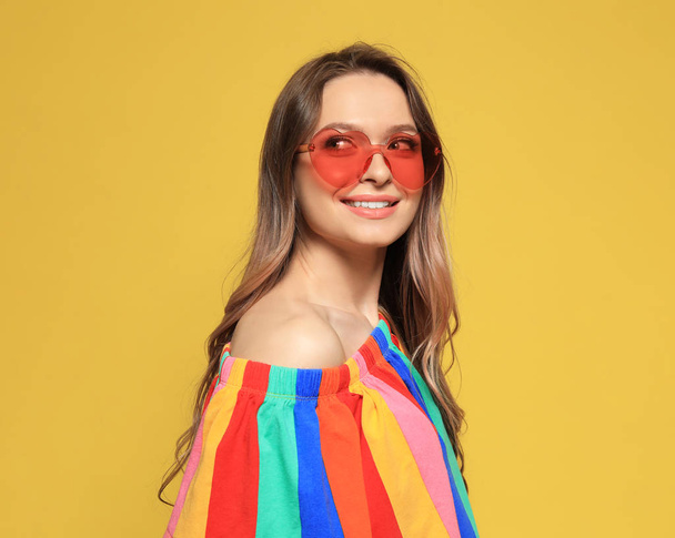Portrait of beautiful young woman with heart shaped sunglasses on color background - Фото, изображение