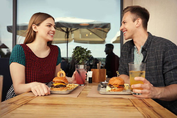 Young happy couple with burgers in street cafe - Fotoğraf, Görsel