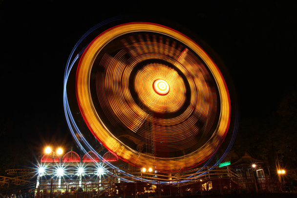 Колесо обозрения в движении освещено ночью
 - Фото, изображение