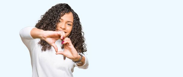 Young beautiful woman with curly hair wearing turtleneck sweater smiling in love showing heart symbol and shape with hands. Romantic concept. - Photo, Image
