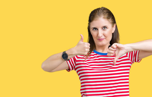 Middle age mature woman wearing casual t-shirt over isolated background Doing thumbs up and down, disagreement and agreement expression. Crazy conflict - Photo, Image
