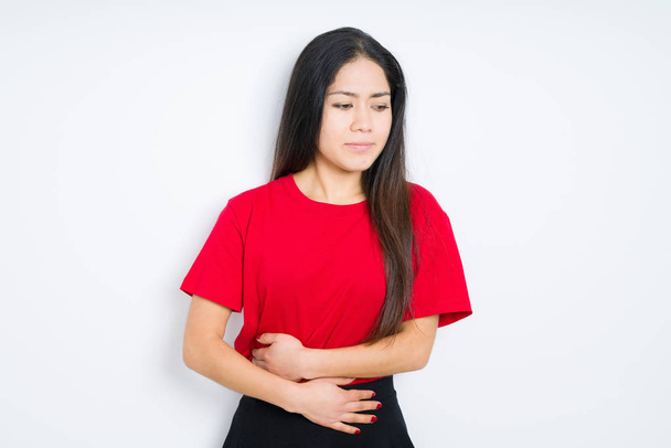 Beautiful brunette woman wearing red t-shirt over isolated background with hand on stomach because nausea, painful disease feeling unwell. Ache concept. - Fotoğraf, Görsel