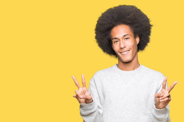 Young african american man with afro hair wearing sporty sweatshirt smiling looking to the camera showing fingers doing victory sign. Number two. - Photo, Image