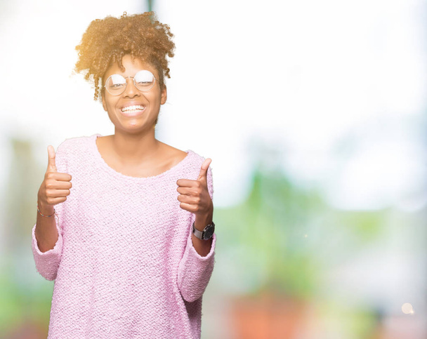 Bella giovane donna afroamericana con gli occhiali su sfondo isolato segno di successo facendo gesto positivo con la mano, pollici in su sorridente e felice. Guardando la macchina fotografica con espressione allegra, gesto vincitore
. - Foto, immagini