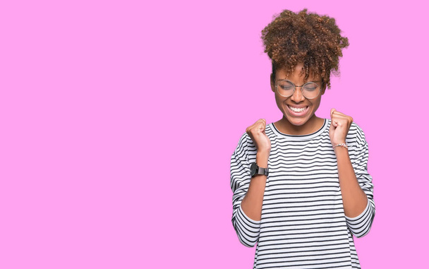 Kaunis nuori afrikkalainen amerikkalainen nainen yllään lasit yli eristetty tausta innoissaan menestystä aseiden esille juhlii voittoa hymyillen. Voittajan käsite
. - Valokuva, kuva