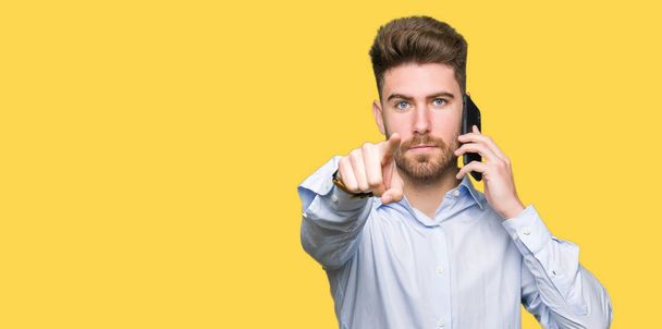 Young handsome man business talking on smartphone pointing with finger to the camera and to you, hand sign, positive and confident gesture from the front - Photo, Image