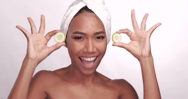 Close-up portret van een mooie lachende vrouw met een schone huid die de ogen bedekt met komkommers die op een witte achtergrond zijn geïsoleerd. Schoonheidsbehandelingen en cosmetica Spa Therapy concept - Video