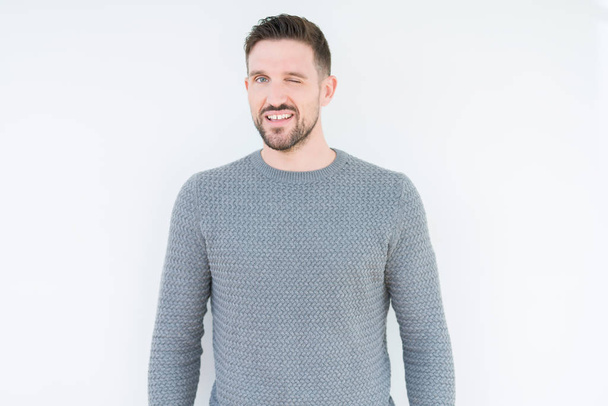 Young handsome man wearing casual sweater over isolated background winking looking at the camera with sexy expression, cheerful and happy face. - Фото, изображение