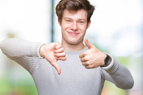 Young handsome man wearing winter sweater over isolated background Doing thumbs up and down, disagreement and agreement expression. Crazy conflict - Fotó, kép