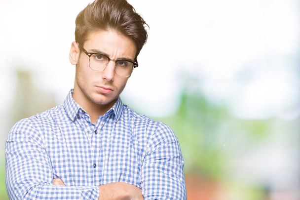 Young handsome man wearing glasses over isolated background skeptic and nervous, disapproving expression on face with crossed arms. Negative person. - Fotografie, Obrázek