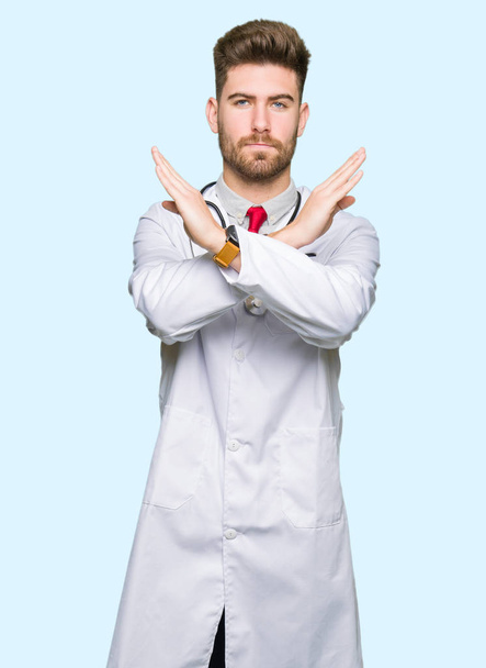 Jeune beau médecin homme vêtu d'un manteau médical expression de rejet croisant les bras faisant signe négatif, visage en colère
 - Photo, image