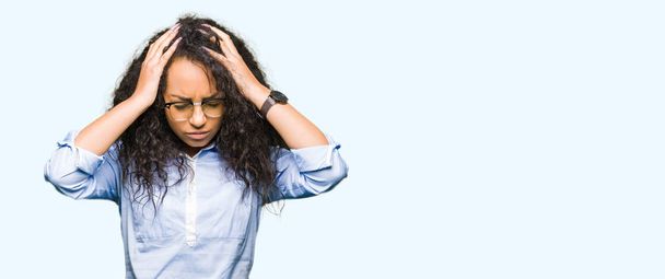 junge schöne Business-Girl mit lockigem Haar und Brille leiden unter Kopfschmerzen verzweifelt und gestresst, weil Schmerzen und Migräne. Hände auf den Kopf. - Foto, Bild