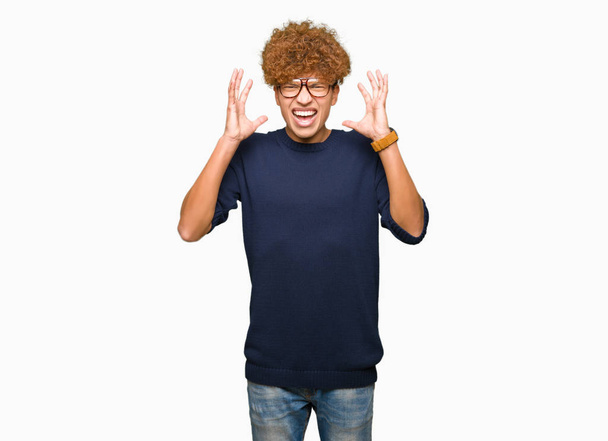 Young handsome man with afro wearing glasses celebrating mad and crazy for success with arms raised and closed eyes screaming excited. Winner concept - Photo, Image