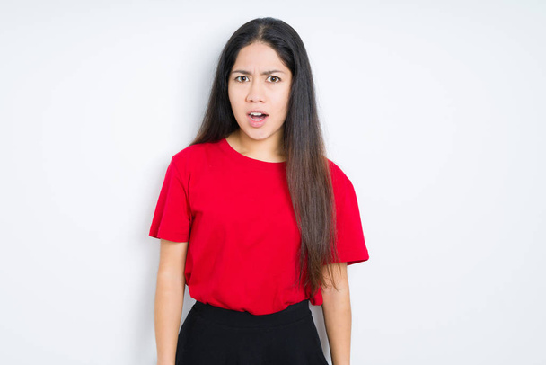 schöne brünette Frau trägt rotes T-Shirt über isoliertem Hintergrund im Schockgesicht, sieht skeptisch und sarkastisch aus, überrascht mit offenem Mund - Foto, Bild