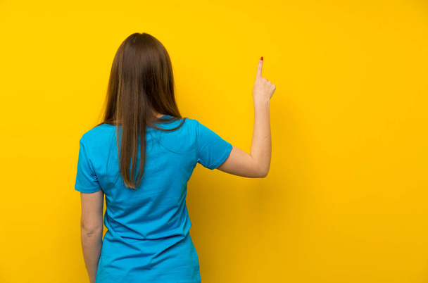 Young woman with blue shirt pointing back with the index finger - Foto, afbeelding