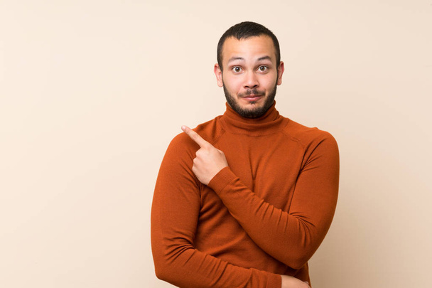 Colombian man with turtleneck sweater pointing to the side to present a product - Photo, Image