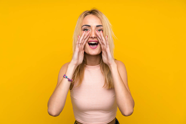 Jonge blonde vrouw over geïsoleerde gele muur schreeuwen met mond wijd open - Foto, afbeelding