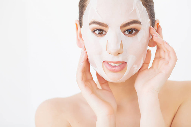 Mooie jonge vrouw krijgt facial klei masker in spa, liggend met komkommers op ogen - Foto, afbeelding