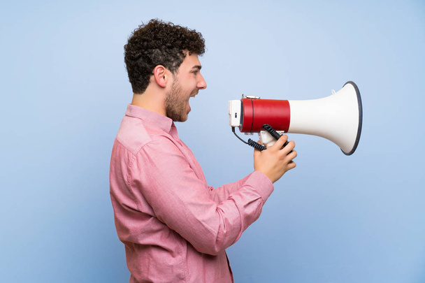 Man with curly hair over isolated blue wall shouting through a megaphone - Foto, Imagen