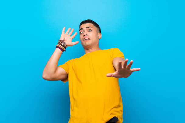Jeune homme avec chemise jaune sur fond bleu isolé nerveux et effrayé
 - Photo, image