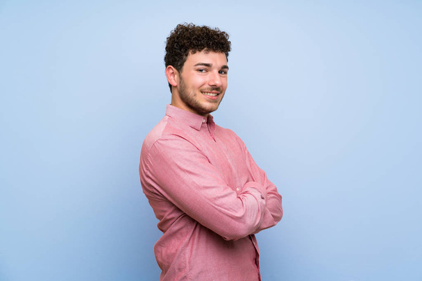 Man with curly hair over isolated blue wall with arms crossed and looking forward - Foto, afbeelding