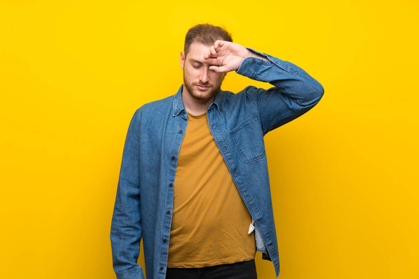 Blonde man over geïsoleerde gele muur met moe en ziek expressie - Foto, afbeelding