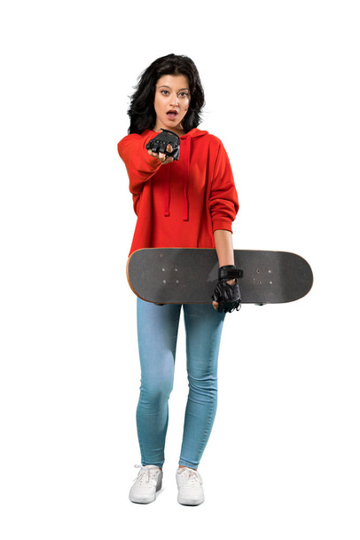 A full-length shot of a Young skater woman surprised and pointing front over isolated white background - Фото, зображення