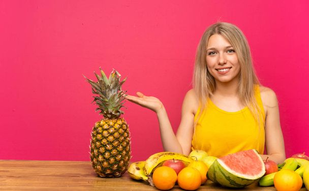 junge blonde Frau mit vielen Früchten hält Kopierraum imaginär auf der Handfläche - Foto, Bild