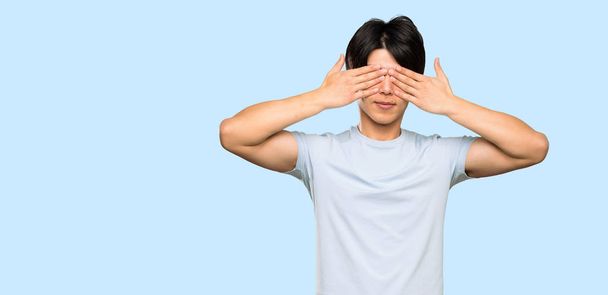 Asian man with blue shirt covering eyes by hands over isolated blue background - Photo, Image