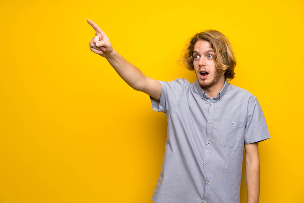 Blonde man over isolated yellow background pointing away - Foto, immagini