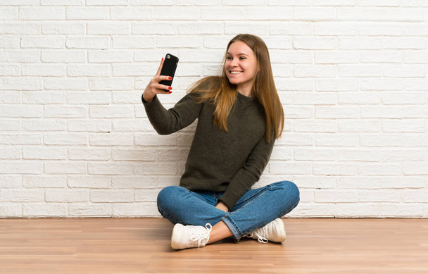 Młoda kobieta siedząca na podłodze i robiąca selfie - Zdjęcie, obraz