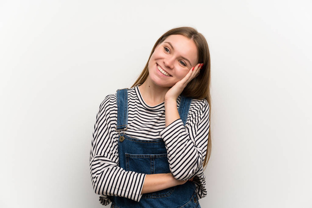 Young woman in dungarees over white wall laughing - Φωτογραφία, εικόνα