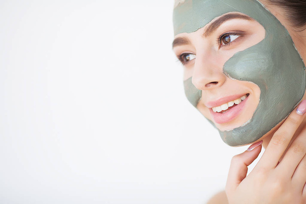 Уход за кожей. Молодая женщина в косметической глиняной маске держит огурец в своей ванной
 - Фото, изображение