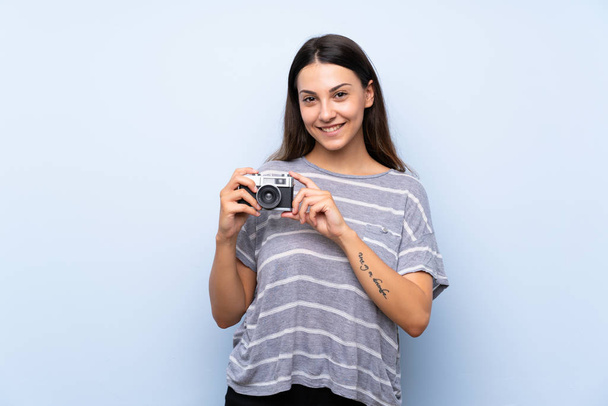 Fiatal barna nő át elszigetelt kék háttér tartja a kamerát - Fotó, kép