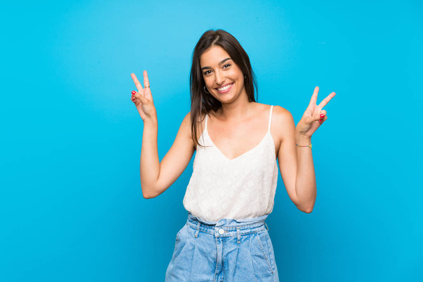 jonge vrouw over geïsoleerde blauwe achtergrond tonen overwinning teken met beide handen - Foto, afbeelding