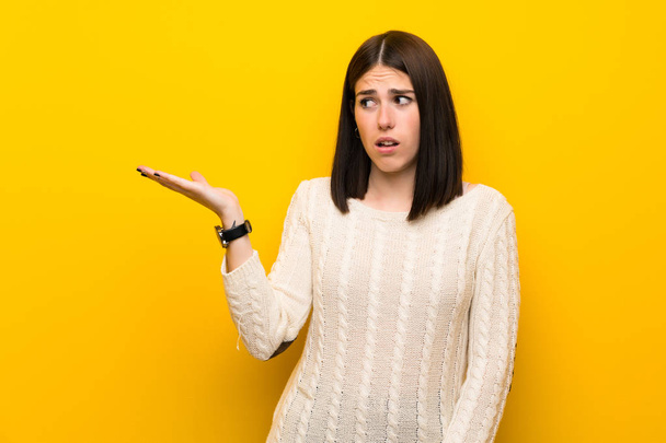 Young woman over isolated yellow wall making doubts gesture - Foto, afbeelding