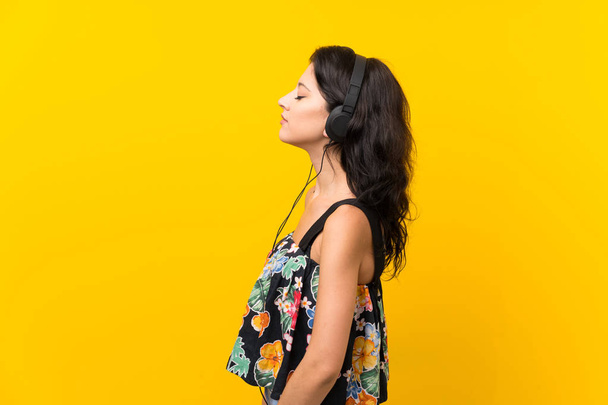 Mladá žena na izolovaném žlutém pozadí poslech hudby se sluchátky - Fotografie, Obrázek
