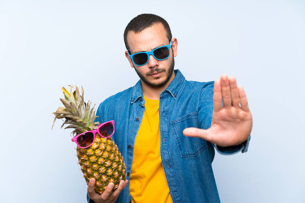 Kolumbiai férfi gazdaság egy ananász a napszemüveg hogy stop gesztus a kezét - Fotó, kép