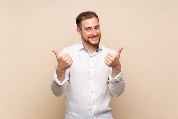 Blonde man over geïsoleerde achtergrond met duim omhoog gebaar en glimlachend - Foto, afbeelding