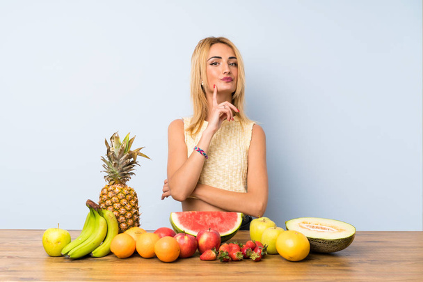 Jonge blonde vrouw met veel fruit denken een idee - Foto, afbeelding