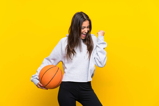 Young woman playing basketball over isolated yellow background celebrating a victory - Fotoğraf, Görsel